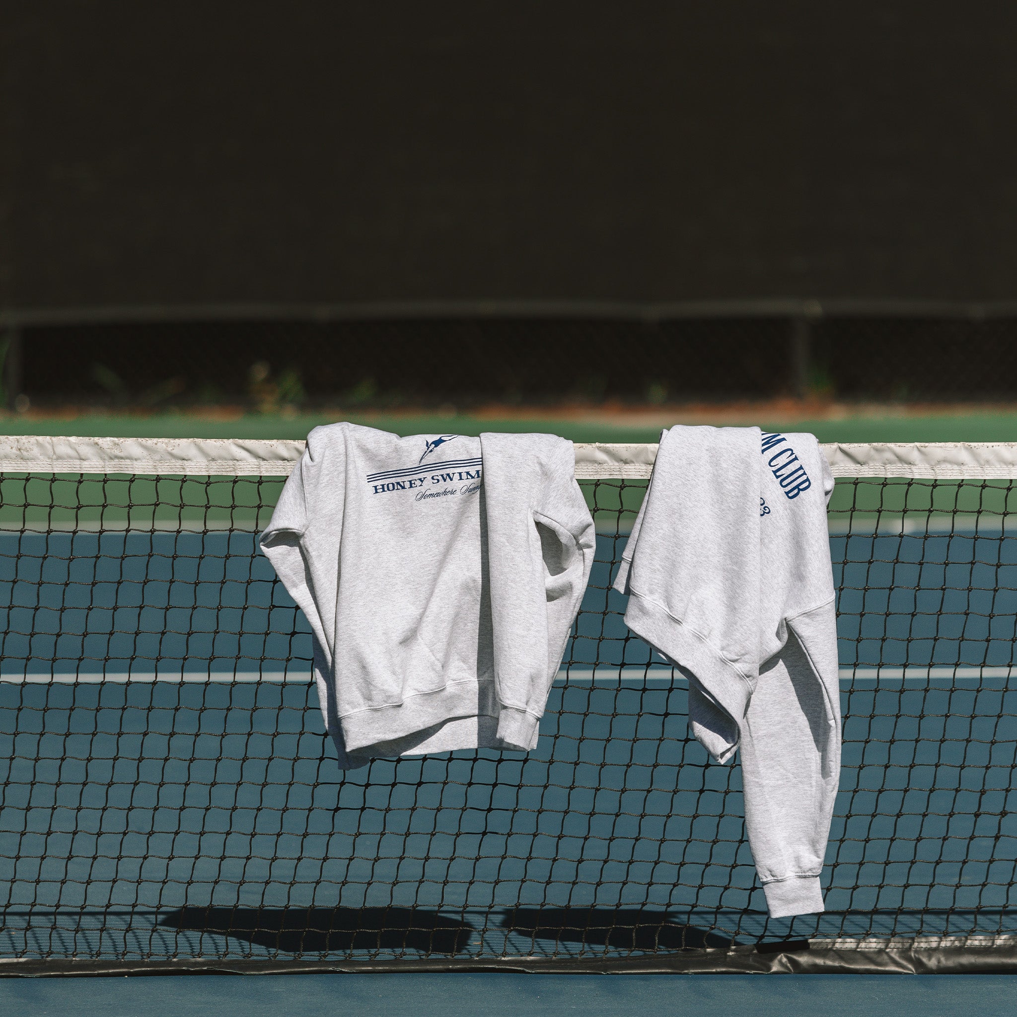 honey swim crewnecks leaning over a tennis court along the beaches on 30A Florida