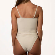 A person with long hair models the Honey Swim Champagne Shimmer One-Piece, featuring adjustable spaghetti straps and high-cut leg openings, set against a plain white background.