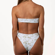 Rear view of a model wearing the Serenity Cinched Bandeau Set by Honey Swim, displaying a white bikini with gold patterns. It includes a strapless top and high-waisted bottoms, all set against a plain white background.