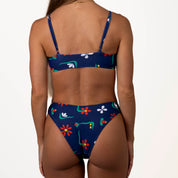 Rear view of a person in the Paradiso Bralette Set by Honey Swim; it’s a blue bikini with colorful floral patterns and adjustable straps, set against a plain white background.