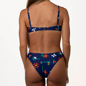 A person models the Paradiso Underwire Top by Honey Swim, featuring a blue bikini with enhanced support and a vibrant floral print, set against a plain white background.