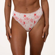 A person wears Honey Swims Isla Ribbed high-waisted bikini bottoms with a red tropical print of palm trees and abstract shapes, offering supportive fit against a plain white background.
