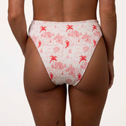 A person in Honey Swims Isla Ribbed High Waisted Bottoms with a red and white tropical print of palm trees and island scenes enjoys a supportive fit with moderate coverage against a plain white background.