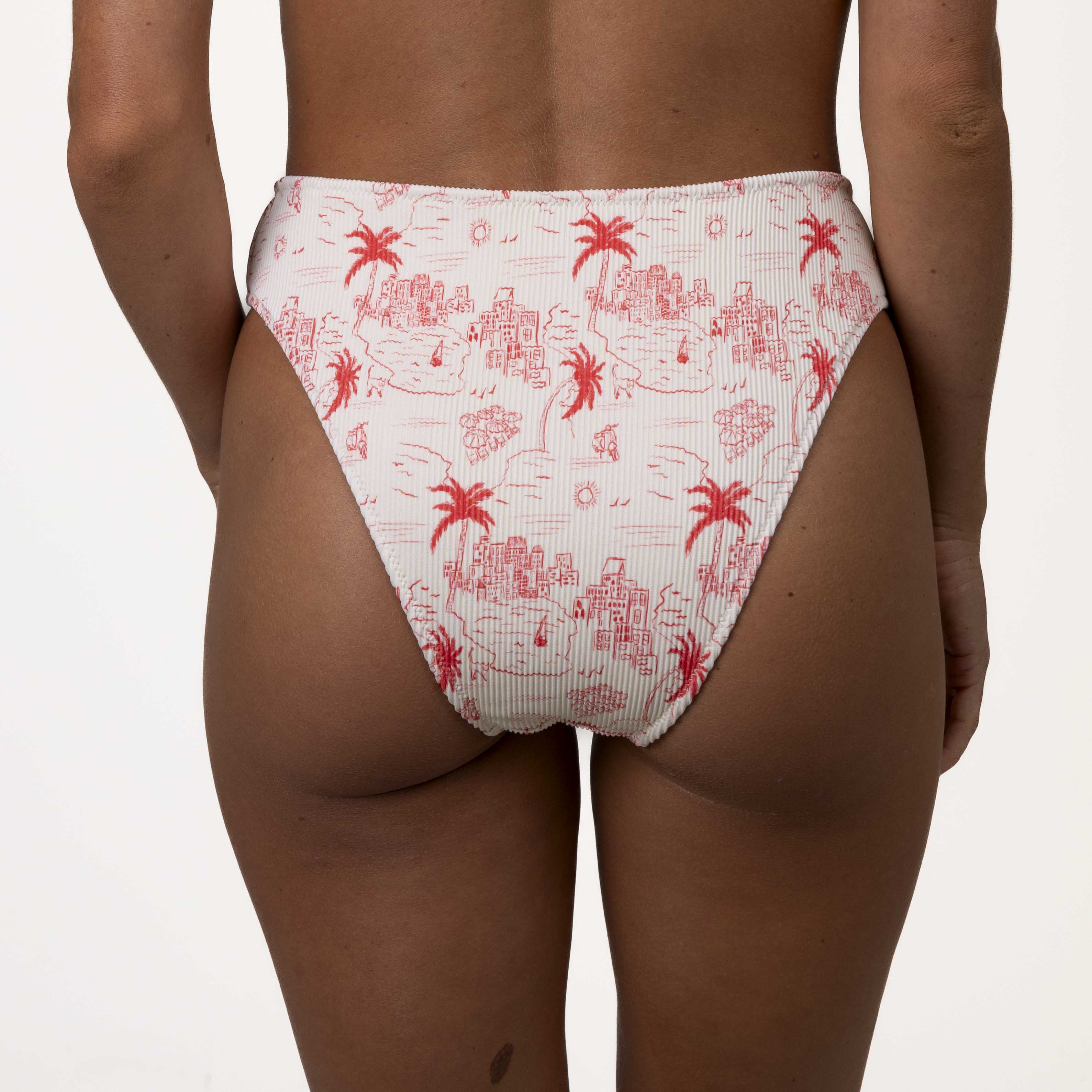 A person in Honey Swims Isla Ribbed High Waisted Bottoms with a red and white tropical print of palm trees and island scenes enjoys a supportive fit with moderate coverage against a plain white background.