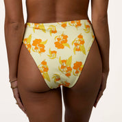 Person flaunts the Sunni High Waisted Bottoms from Honey Swim, featuring a supportive fit and moderate coverage in a yellow with orange floral pattern, paired with bracelets on one wrist against an off-white background.