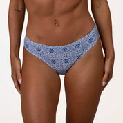 Close-up of a persons lower torso in Honey Swims Mykonos Squareneck Set blue mosaic tile print bikini bottoms, highlighting their tanned skin against a plain white background.