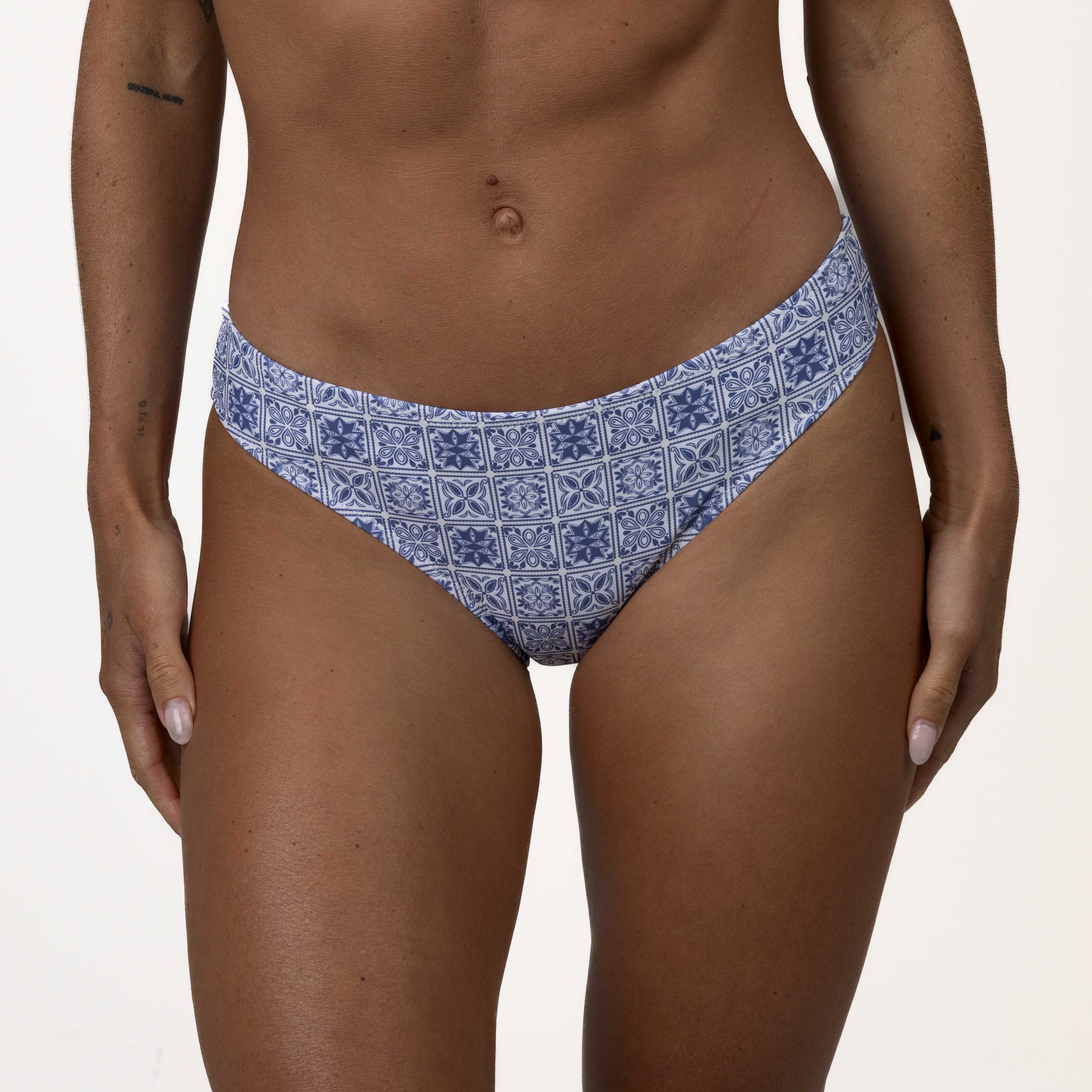 Close-up of a persons lower torso in Honey Swims Mykonos Squareneck Set blue mosaic tile print bikini bottoms, highlighting their tanned skin against a plain white background.