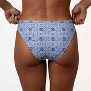 A person in a Honey Swim Mykonos Squareneck Set with a blue mosaic tile print stands against a white background, adjusting the waistband to highlight its supportive fit.