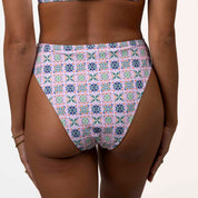 The Honey Swim Capri Bandeau Set showcases a colorful geometric pattern with floral motifs in purple, pink, and blue squares. The image highlights the lower back and bottom.