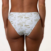 A person models Honey Swims Serenity full coverage bottoms, featuring a smooth texture and printed design of buildings, trees, and bicycles, shown from the back against a plain background.