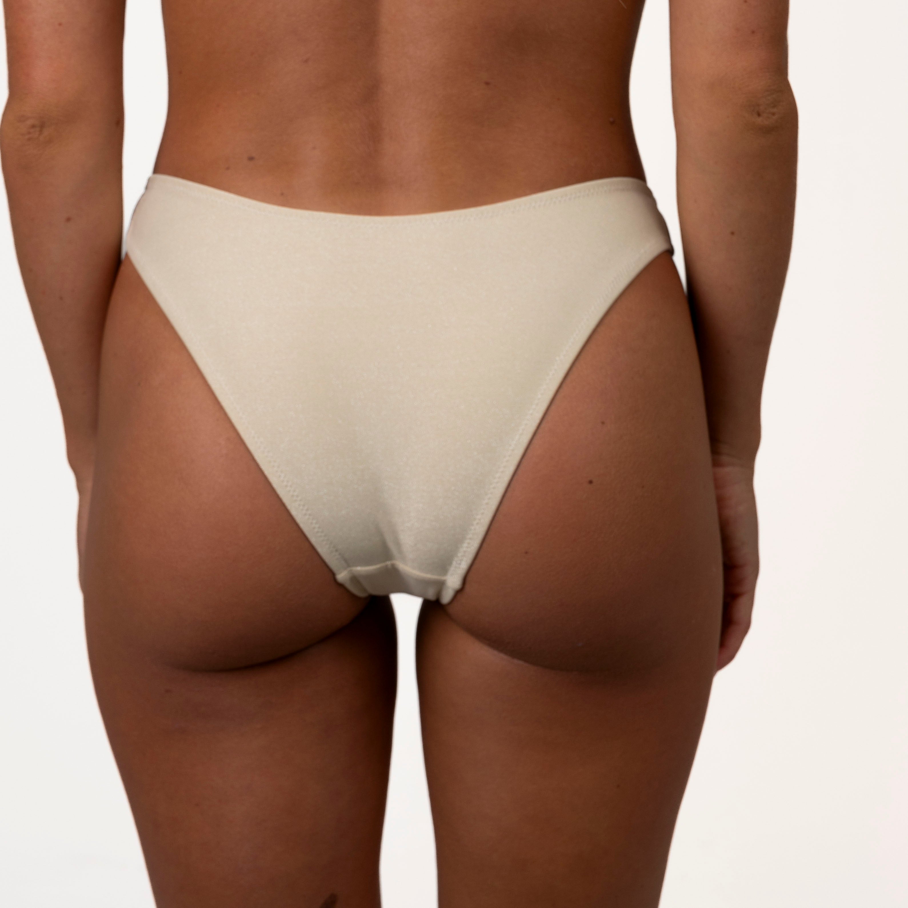 A person is shown from behind in a Honey Swim Champagne Shimmer Bandeau Set against a plain backdrop, highlighting the swimwear and their skin tone.