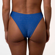 A model showcases Honey Swims Azure Shimmer Bralette Set, highlighted by its striking design and subtle elegance, against a plain white background.