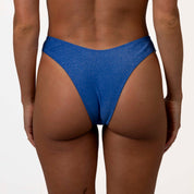 A person models Honey Swims Azure Shimmer Bralette Set, showcasing the sparkly blue bikini bottoms against a plain white backdrop.