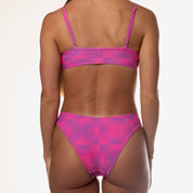 A person is wearing the Starlight Bralette Set by Honey Swim, showcasing its pink sunburst patterns and adjustable straps against a plain white background, viewed from the back.