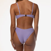 A person stands against a white backdrop wearing the Lavender Shimmer Underwire Set by Honey Swim, with their arms relaxed at their sides, highlighting the shimmer of the bikini.