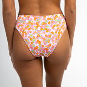 A person wearing Honey Swims Poppy Ribbed Bottoms with orange and pink florals stands against a white background, bracelet on left wrist, offering full coverage in vivid style.