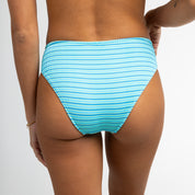 A person models Honey Swims Lani Ribbed Bottoms in blue and white stripes, with cheeky coverage, standing back to the camera against a plain white background.