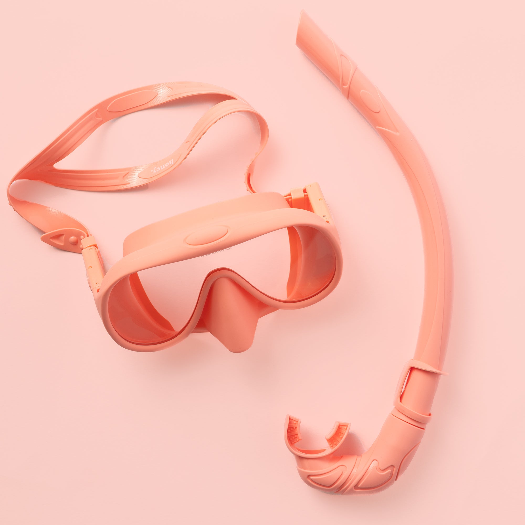 The Honey Snorkel Kit by Honey Swim includes a peach snorkel set with panoramic goggles, adjustable strap, a curved tube snorkel, and comfy mouthpiece against a peach background.