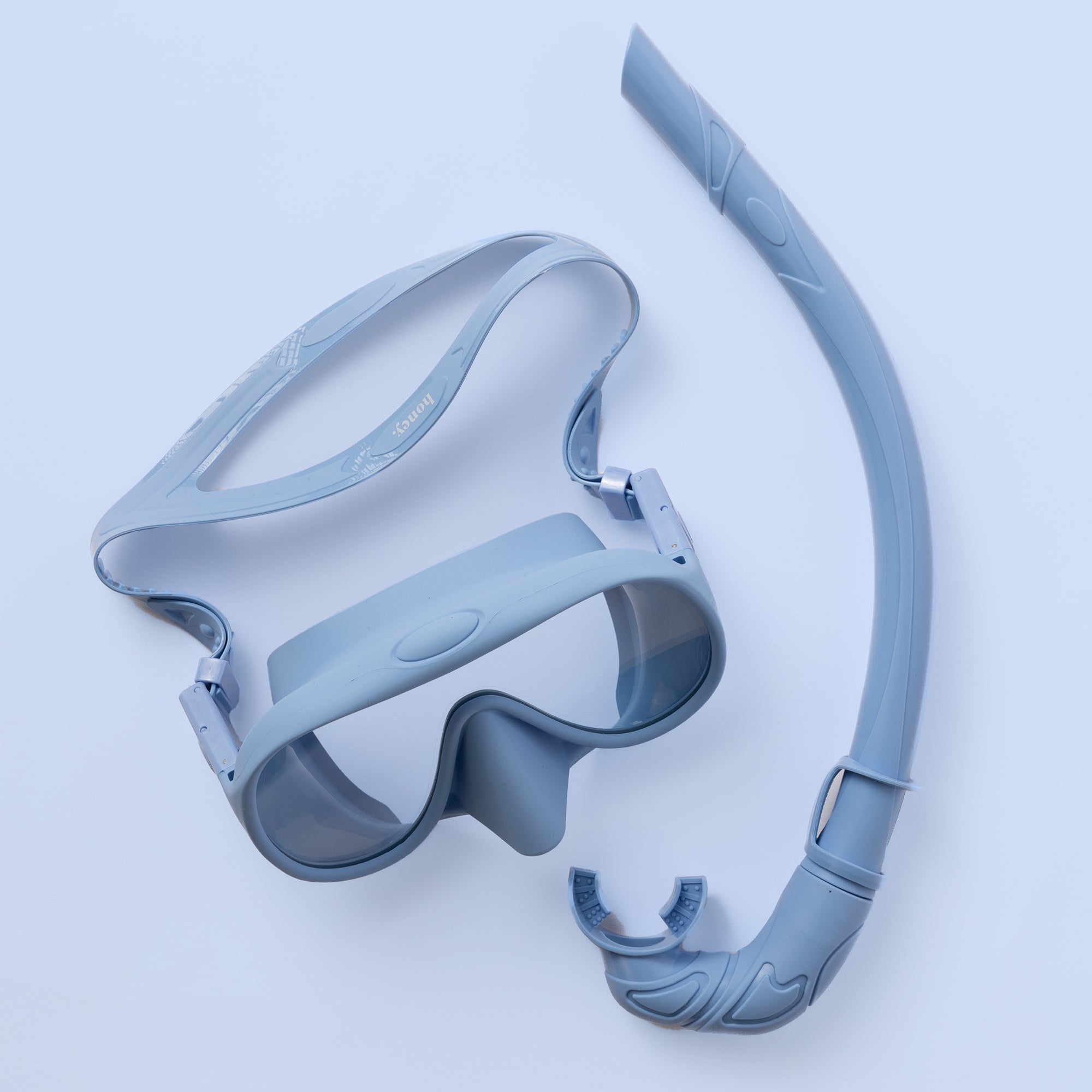 The Honey Swims Honey Snorkel Kit is a sleek, blue set with a single-lens mask and attached snorkel for panoramic views, elegantly placed on a light blue background.