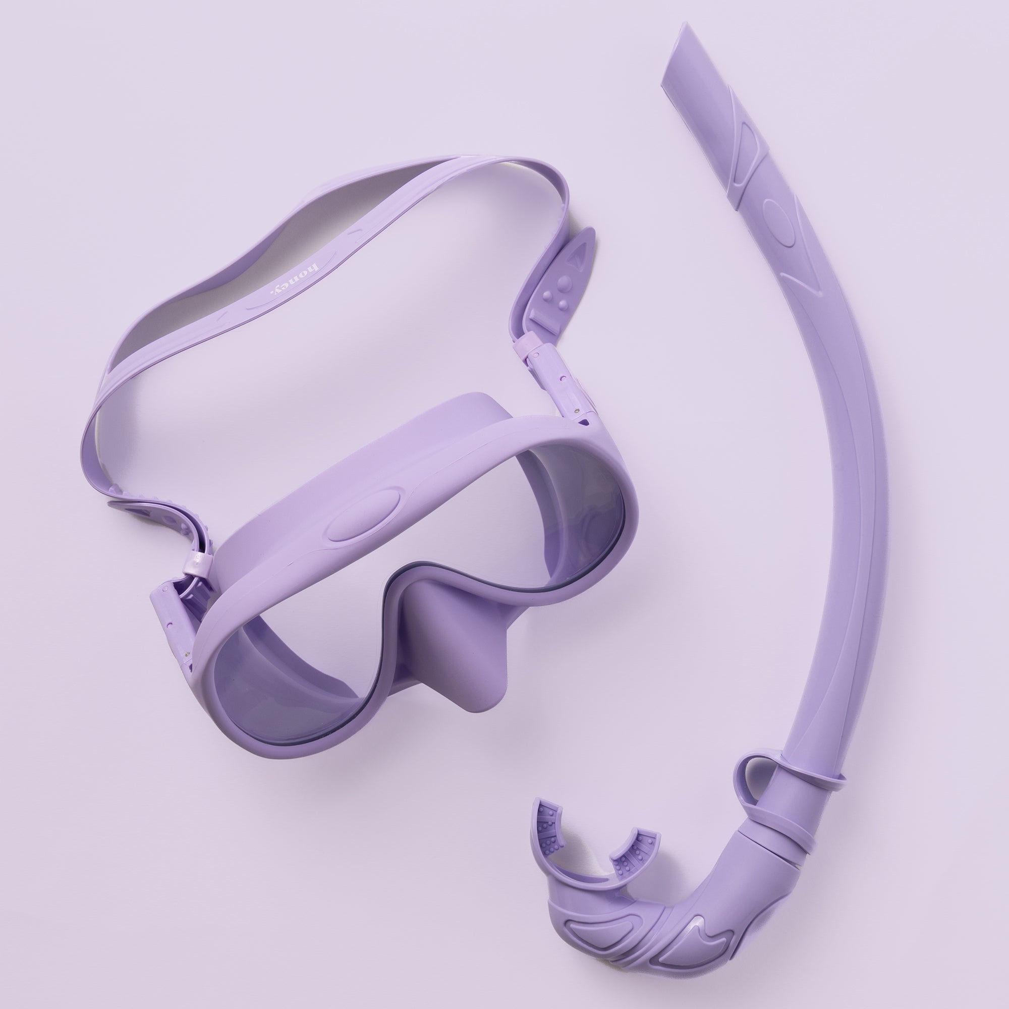 The Honey Snorkel Kit by Honey Swim showcases a purple mask with clear panoramic lenses and a snorkel with a curved design, mouthpiece, and flexible section against a light purple background.