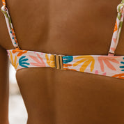 Close-up of a person wearing the Honey Swim Tropics Underwire | Top, featuring adjustable straps and a back clasp. The vibrant tropics pattern showcases hand shapes in orange, blue, and yellow on a light background.