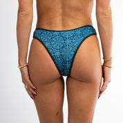 A woman faces away from the camera wearing Honey Swims Bay Ribbed Bottoms and gold jewelry, set against a plain white background.