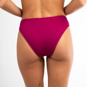 A person models Honey Swim’s Berry Ribbed | Bottoms - All Styles, featuring a classic, high-waisted cheeky cut, facing away from the camera against a plain white background.