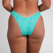 A person wears Honey Swim Drift Ribbed | Classic Bottoms in light green, shown from the back against a plain white background.
