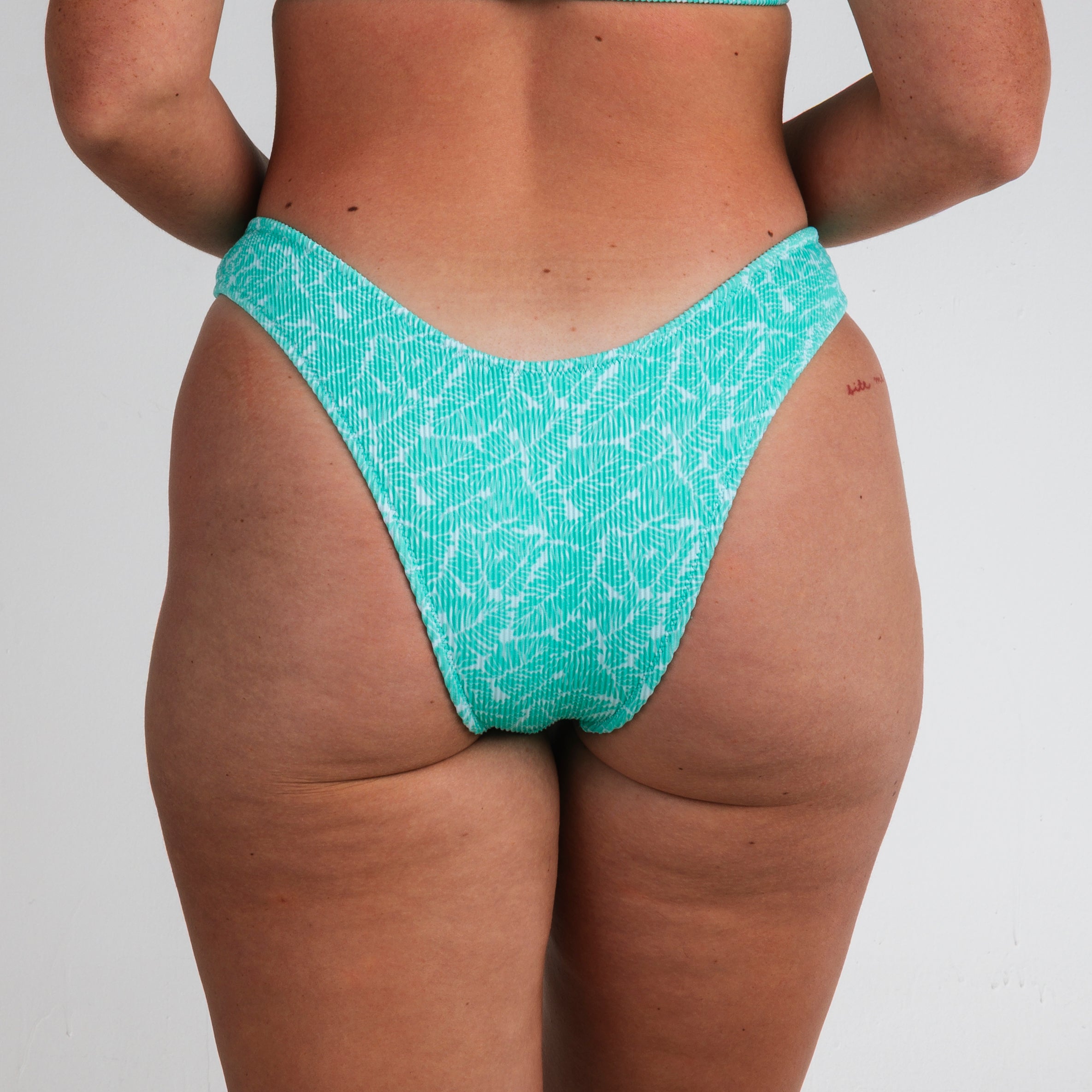 A person wears Honey Swim Drift Ribbed | Classic Bottoms in light green, shown from the back against a plain white background.