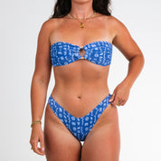 A woman wears the Honey Swim Lagoon Ribbed Bandeau Set, showcasing its blue pattern, circular cutout top, and high-cut bottoms against a plain white background—a vacation essential.