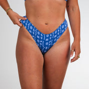 Model wears Honey Swim’s Lagoon Ribbed | Full Coverage Bottoms with white geometric shapes, standing against a plain white background. Only the torso and upper legs are shown, one hand resting on the waistband.