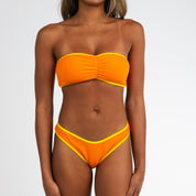 Wearing the Marigold Terry Cinched Bandeau Set by Honey Swim, a person with yellow trim detail poses against a white background—ideal for a stylish beach day.