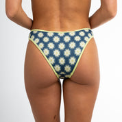 A person is seen from the back wearing Honey Swim Pebble Ribbed | Classic Bottoms, featuring an eclectic daisy print with light yellow contrast piping, against a plain white background.
