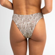 A person is shown from the waist down, wearing Honey Swim’s Rio Ribbed | Bottoms - All Styles with a zebra-print, high-cut design, combining comfort and style against a plain white background.