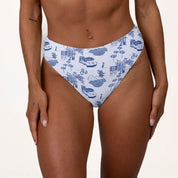 Someone wearing the Honey Swim Amalfi high-waisted bottoms showcasing an intricate blue and white design with bicycles, houses, and trees on a neutral background that highlights its supportive fit.