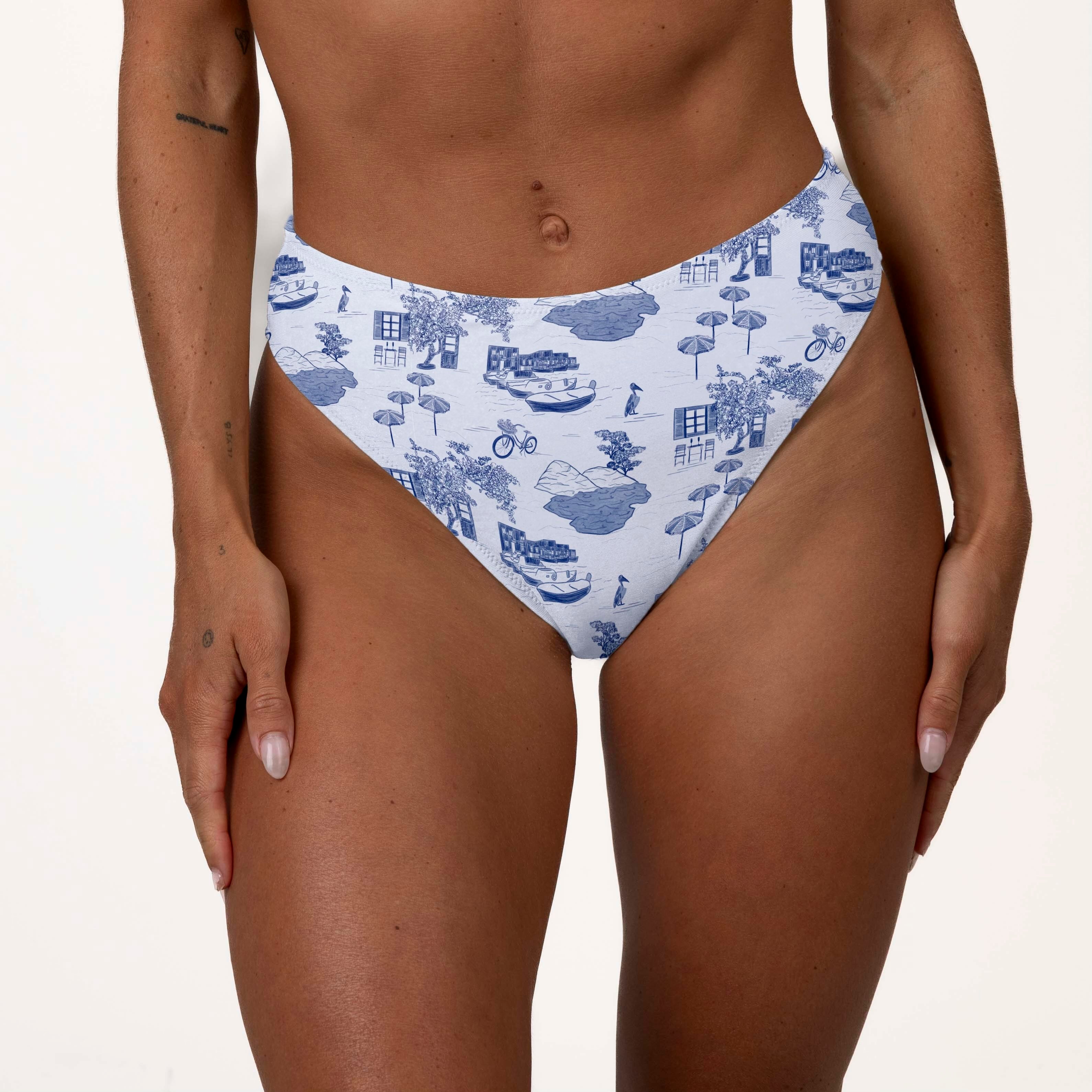 Someone wearing the Honey Swim Amalfi high-waisted bottoms showcasing an intricate blue and white design with bicycles, houses, and trees on a neutral background that highlights its supportive fit.