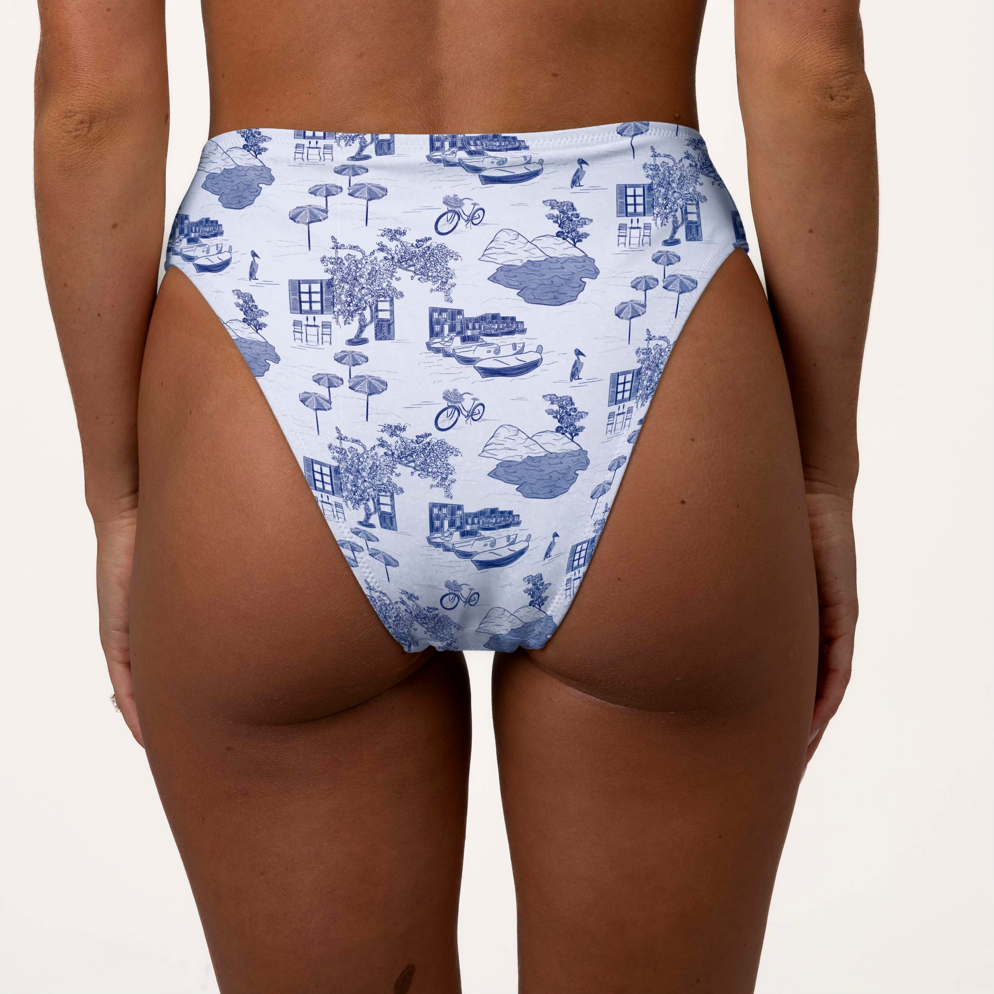 Someone is wearing Honey Swims Amalfi High Waisted Bottoms featuring a blue and white pattern of bicycles, houses, trees, and boats. These bottoms offer moderate coverage and a supportive fit against a plain white background.