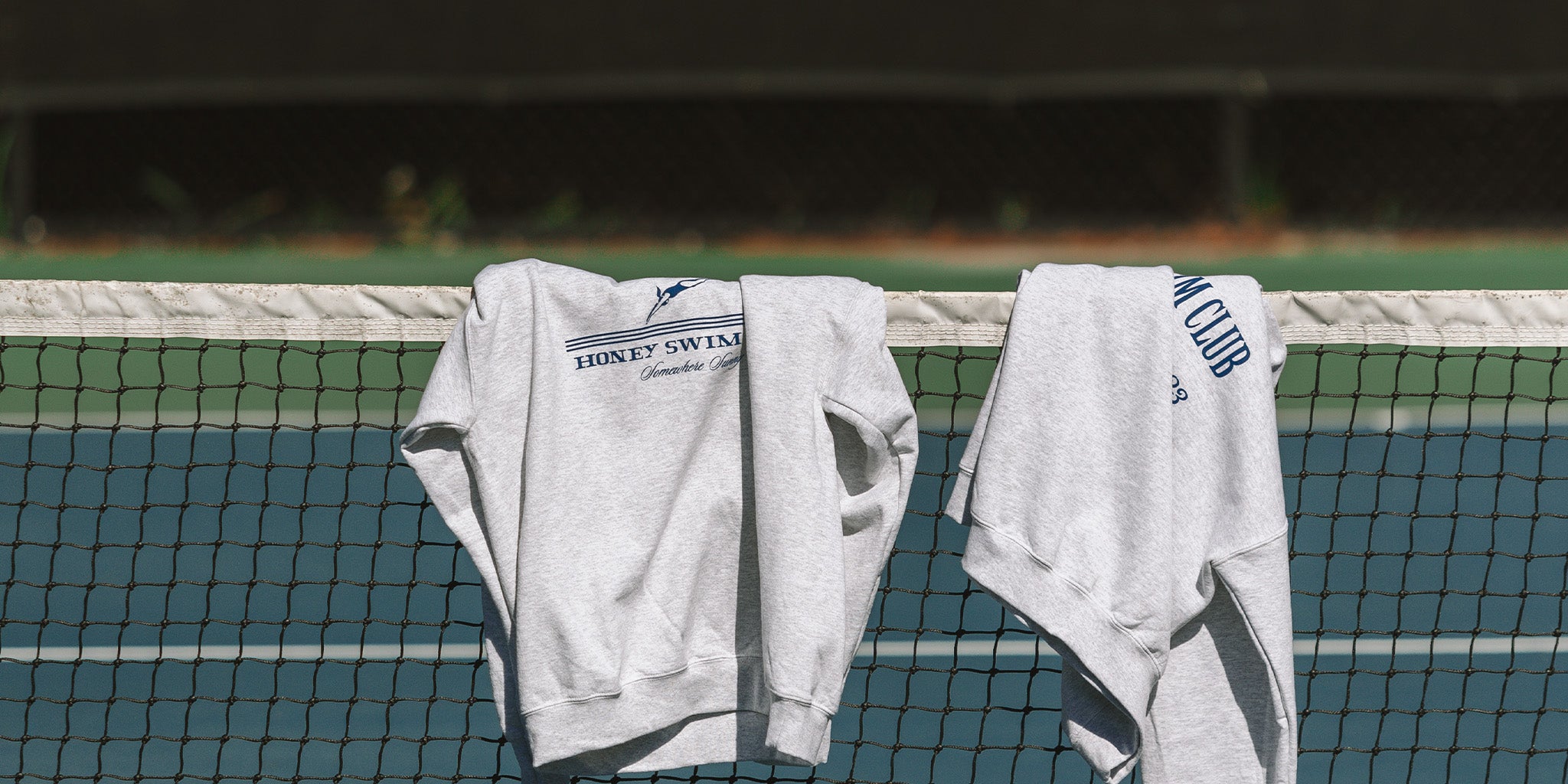 honey swim crewnecks leaning over a tennis court along the beaches on 30A Florida