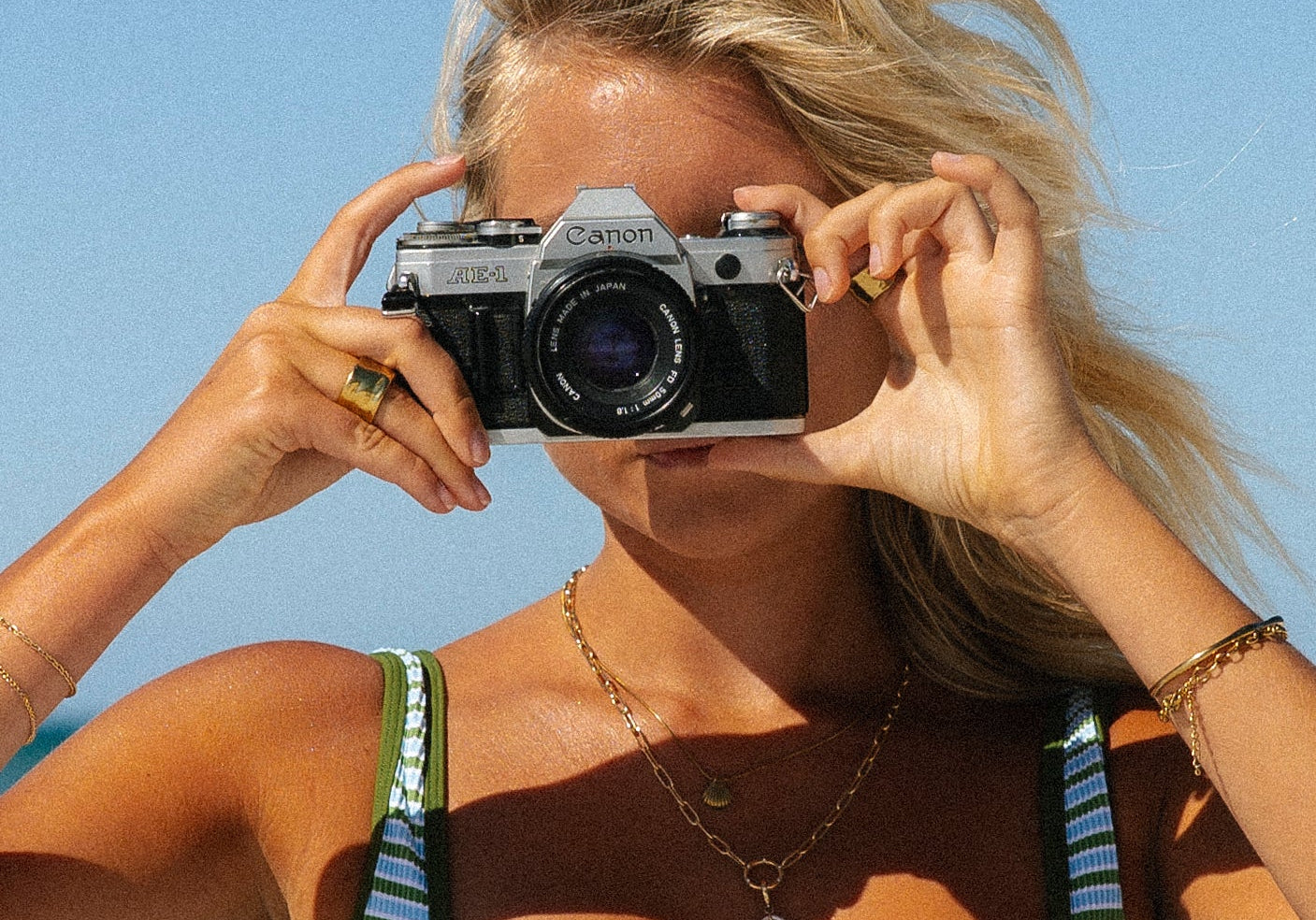 A woman wearing a yellow bikini stands outdoors among lush green tropical plants and palm trees, looking confidently at the camera.