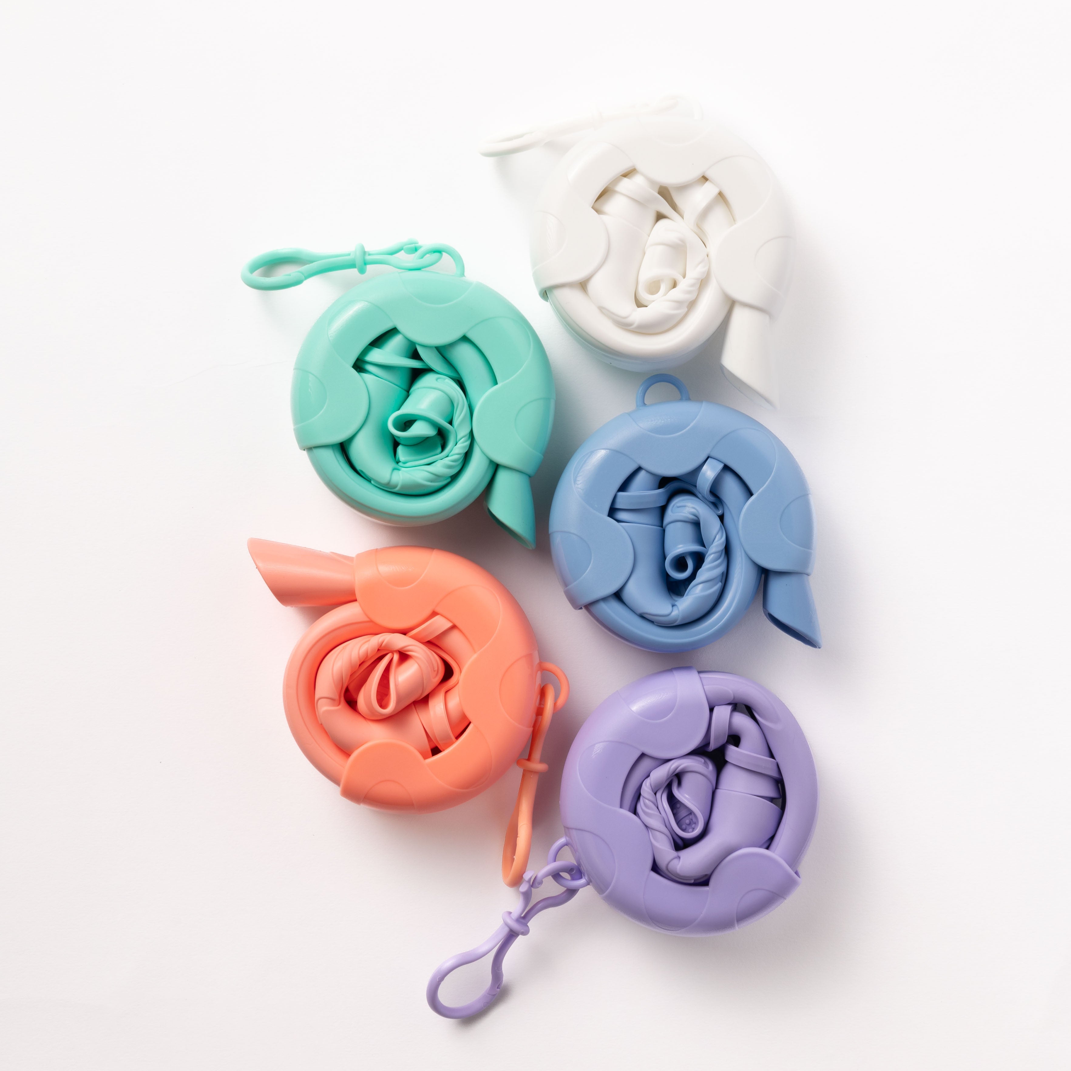 Five vibrant reusable shopping bags neatly folded in circular cases with carabiner clips are set against a white backdrop. The Honey Swim display in white, mint green, blue, orange, and lavender exudes convenience and style.