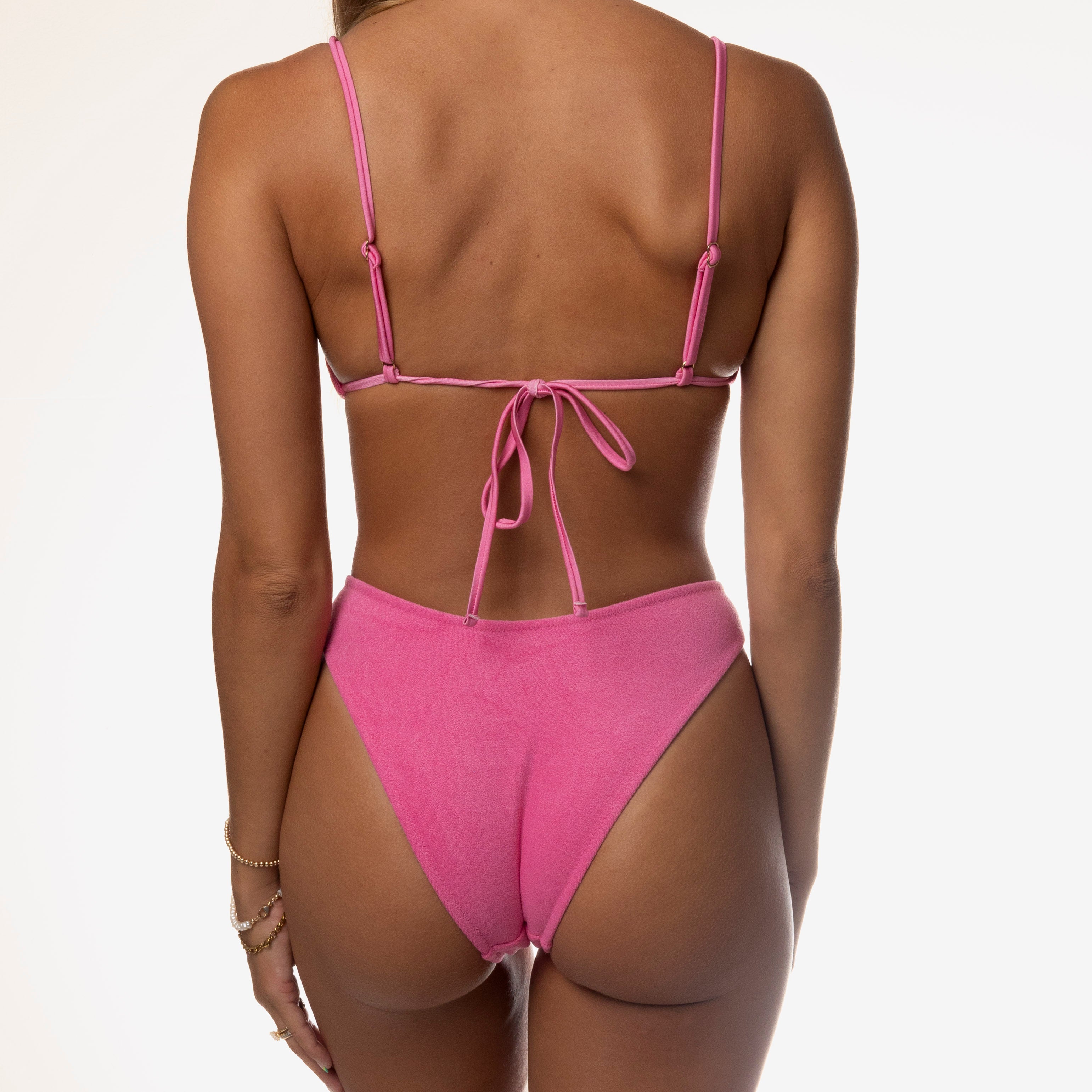 A person models the Flirty Terry Triangle Set by Honey Swim, showcasing its pink bikini with adjustable tieback straps. The super soft terry cloth design subtly highlights their back against a plain white background, ideal for summer sunbathing.