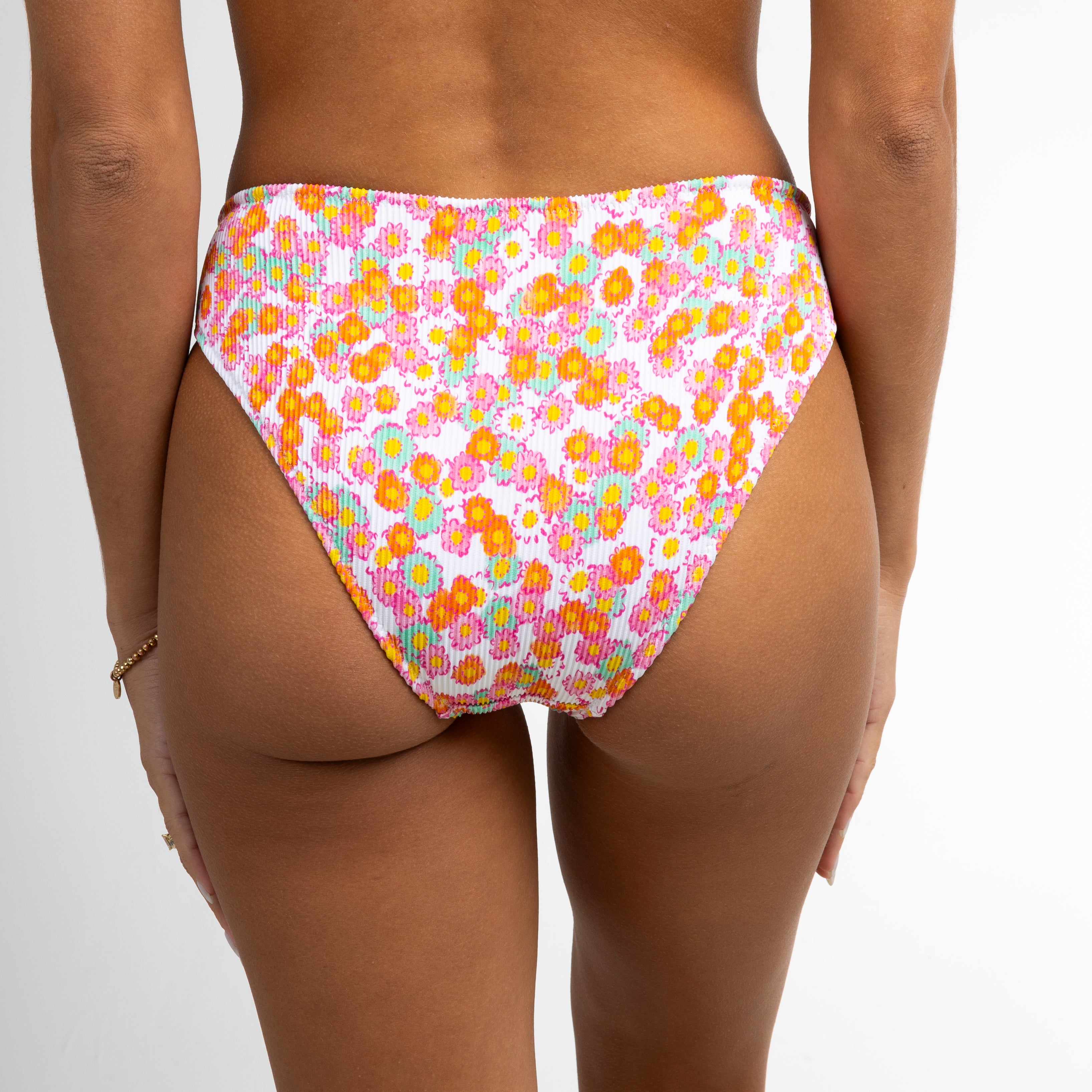A person wearing Honey Swims Poppy Ribbed Bottoms with orange and pink florals stands against a white background, bracelet on left wrist, offering full coverage in vivid style.