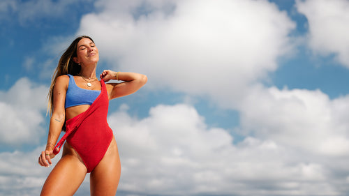 Woman in a blue top and red swimsuit against a blue sky with clouds