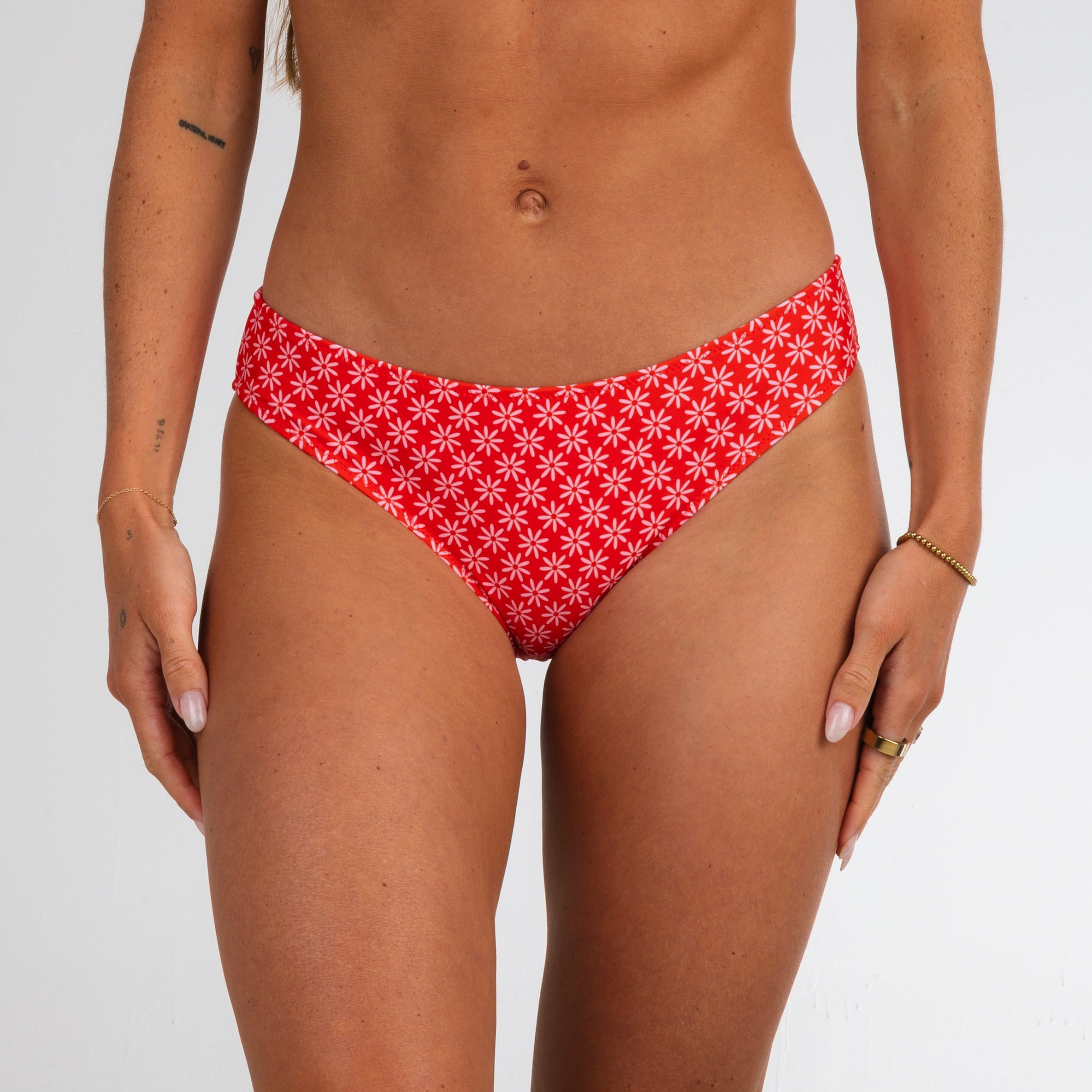 A woman models the Azalea Full Coverage Bottoms by Honey Swim, featuring a flower power print, standing against a plain white background with her arms relaxed at her sides.