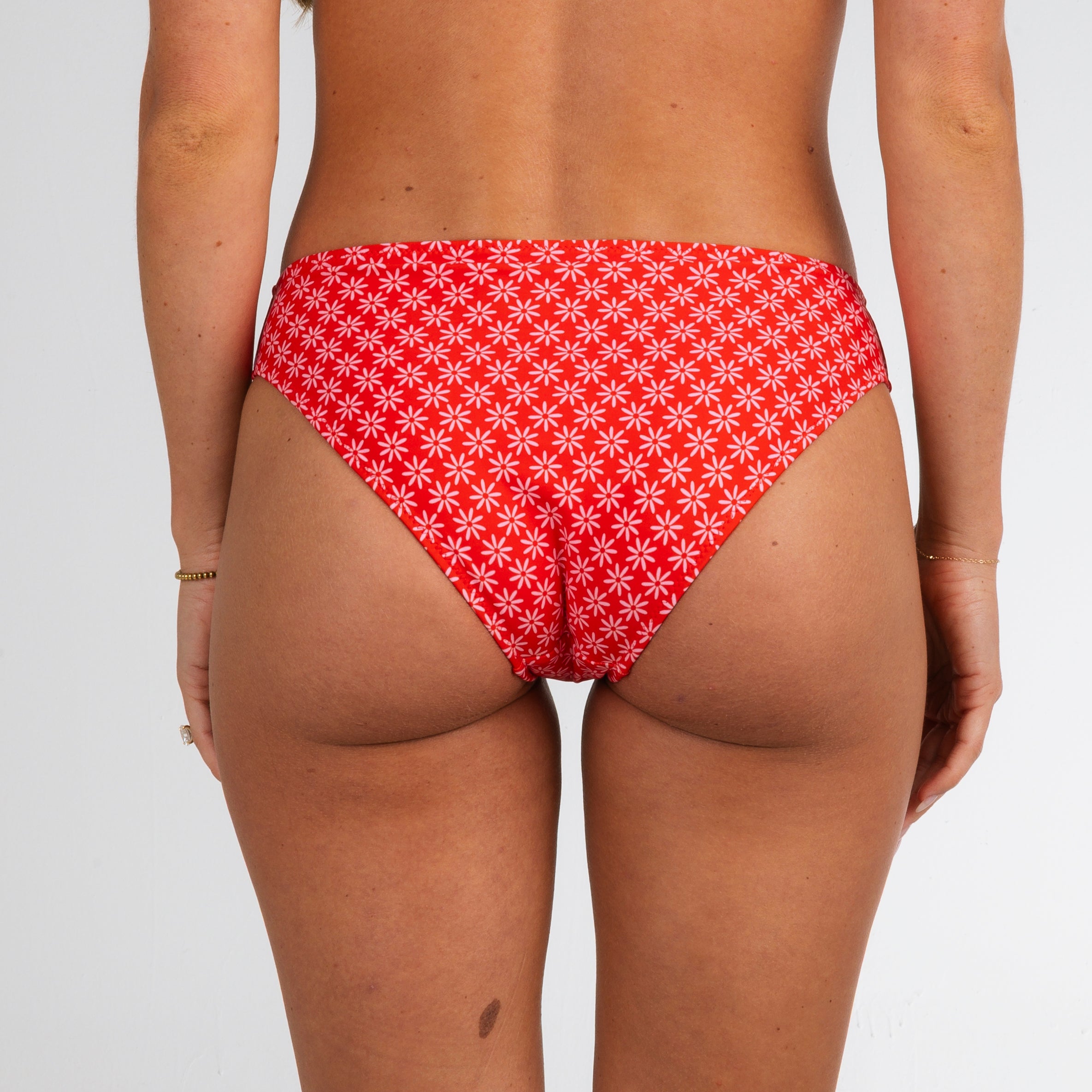 A model showcases the Honey Swim Azalea Full Coverage Bottoms in a bold flower power print, posing with their back to the camera against a plain light background.