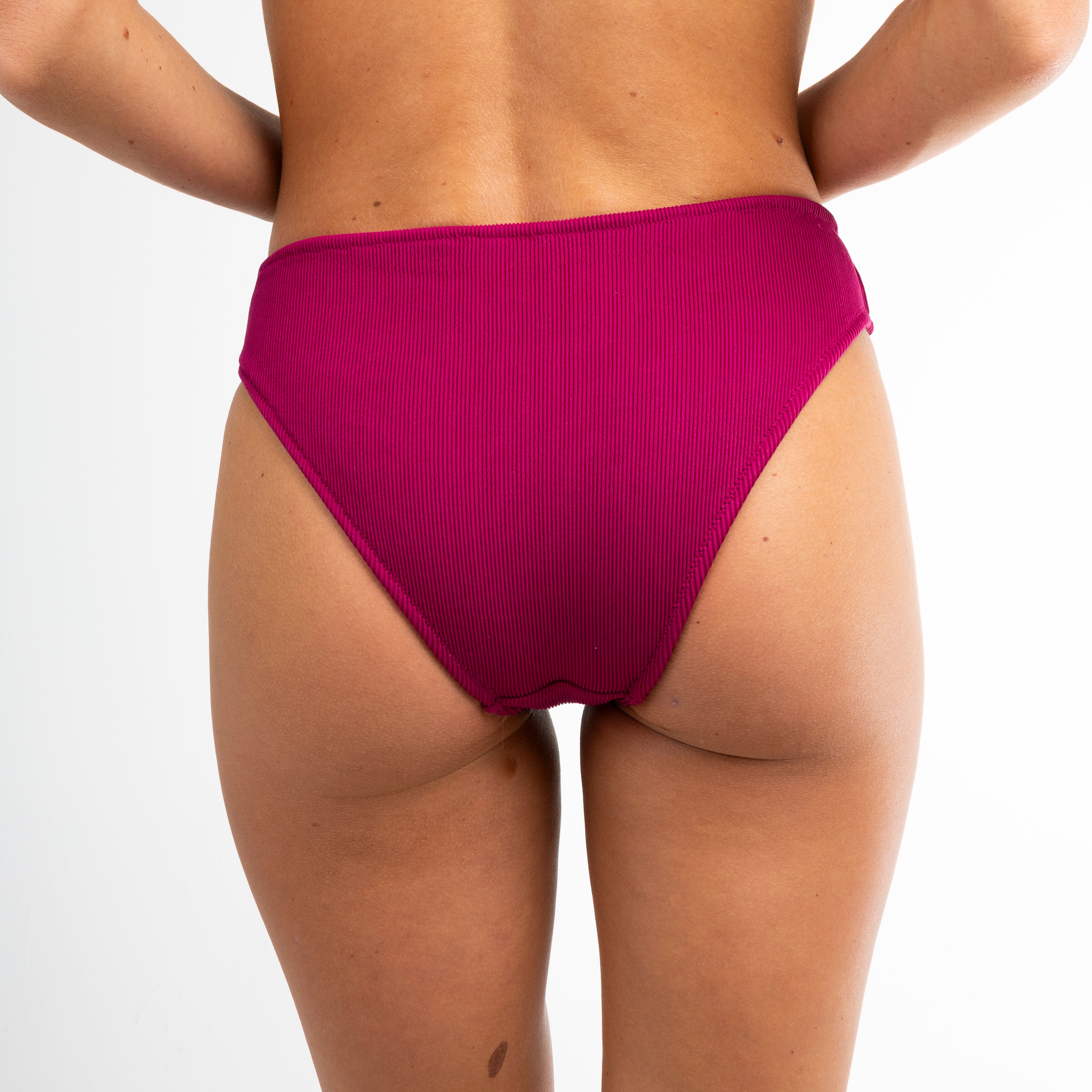A person models Honey Swim’s Berry Ribbed | Bottoms - All Styles, featuring a classic, high-waisted cheeky cut, facing away from the camera against a plain white background.