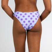 A model showcases Honey Swims Daybreak | Classic Bottoms with a purple starburst pattern on light fabric, perfect for vacation, set against a plain white background.