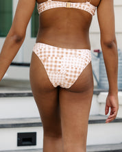 A person in a beige and white patterned bikini stands outdoors, modeling the Harper | Bottoms - All Styles by Honey Swim. Steps and part of a building appear in the background.
