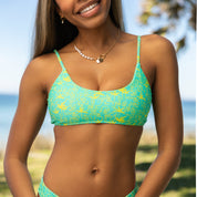 A smiling woman wears the Honey Swim Lush Bralette Set with adjustable straps, standing outdoors near the beach with trees and blue water in the background.