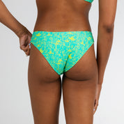 A person models Honey Swim’s Lush | Classic Bottoms in sunshine yellow and teal, shown from the back against a white background—ideal for summer style.